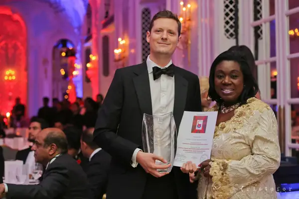 Award winner in black tie holding a glass award and certificate beside a guest in gold at the 2014 bis Awards at The Savoy