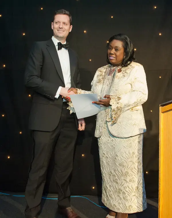 Presenter in black tie and a guest in a cream dress on the awards stage at the 2014 bis Awards at The Savoy