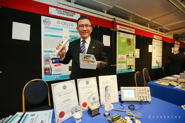 Inventor holding his D-CELLS (Defence Cell Culture System) device in front of its poster at the British Invention Show 2014