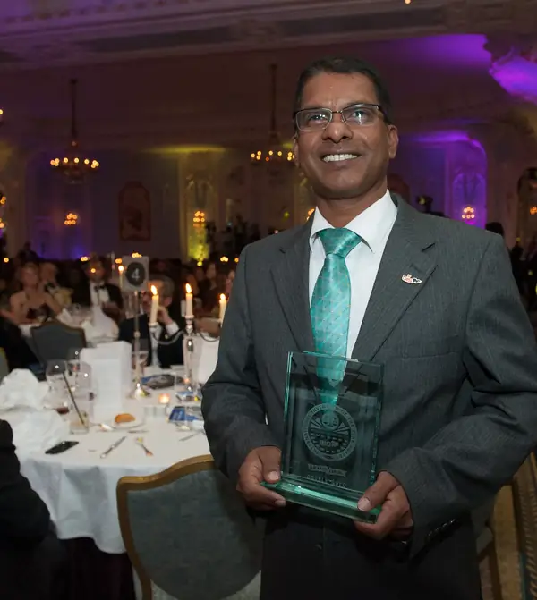 Award winner in a teal tie holding a glass award among the dinner tables at the 2014 bis Awards at The Savoy