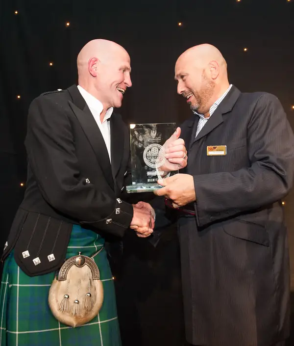 Winner in a kilt receiving a glass award with a handshake at the 2014 bis Awards at The Savoy