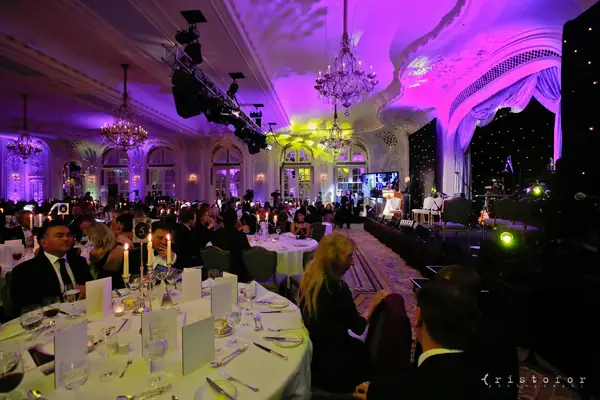 Dinner tables under chandeliers and purple light in the ballroom at the 2014 bis Awards at The Savoy