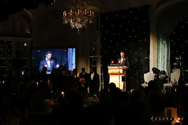 Speaker at a lectern beside a large screen in the darkened ballroom at the 2014 bis Awards at The Savoy