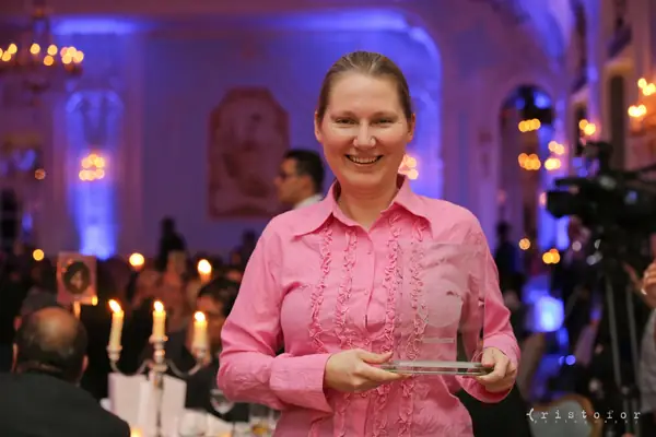Award winner in a pink blouse holding a glass award at the 2014 bis Awards at The Savoy