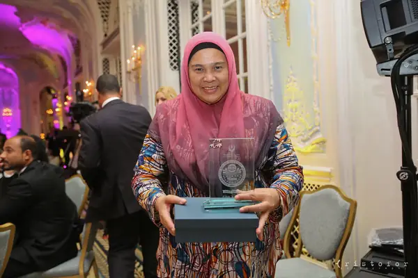 Award winner in a pink headscarf holding a glass award and its box at the 2014 bis Awards at The Savoy