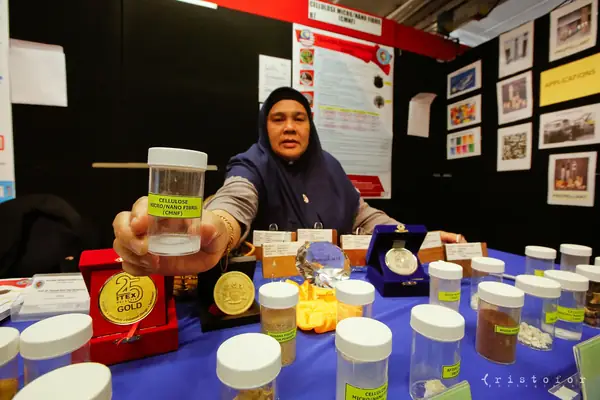 Exhibitor holding a jar of cellulose micro/nano fibrils (CMNF) beside her medals at the British Invention Show 2014