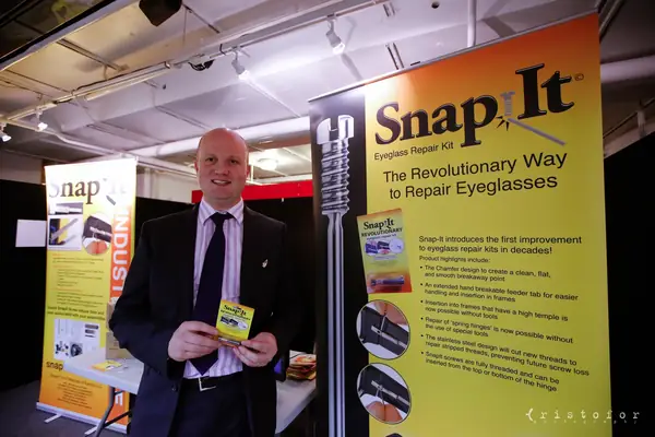 Exhibitor holding a Snap-It eyeglass repair kit in front of its banner at the British Invention Show 2014