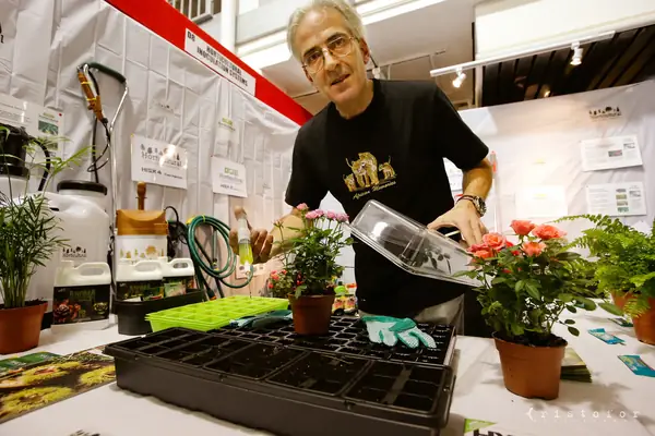 Exhibitor demonstrating a seedling tray among potted flowers at the British Invention Show 2014