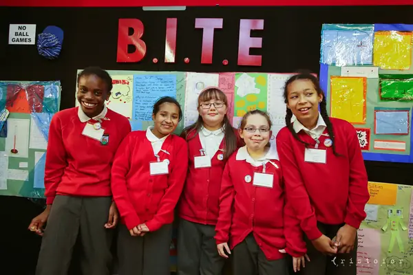 Five pupils in red uniforms in front of the B.I.T.E. display wall at the British Invention Show 2014