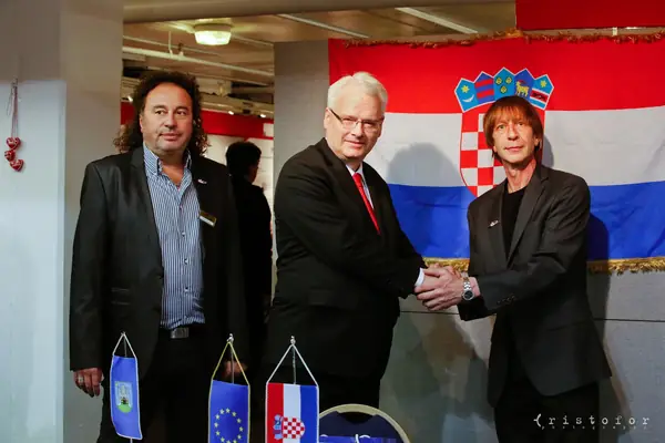 Three men shaking hands in front of a Croatian flag at the British Invention Show 2014