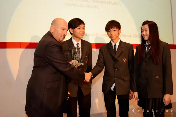 Three school students receiving a glass award with a handshake at the British Invention Awards 2013